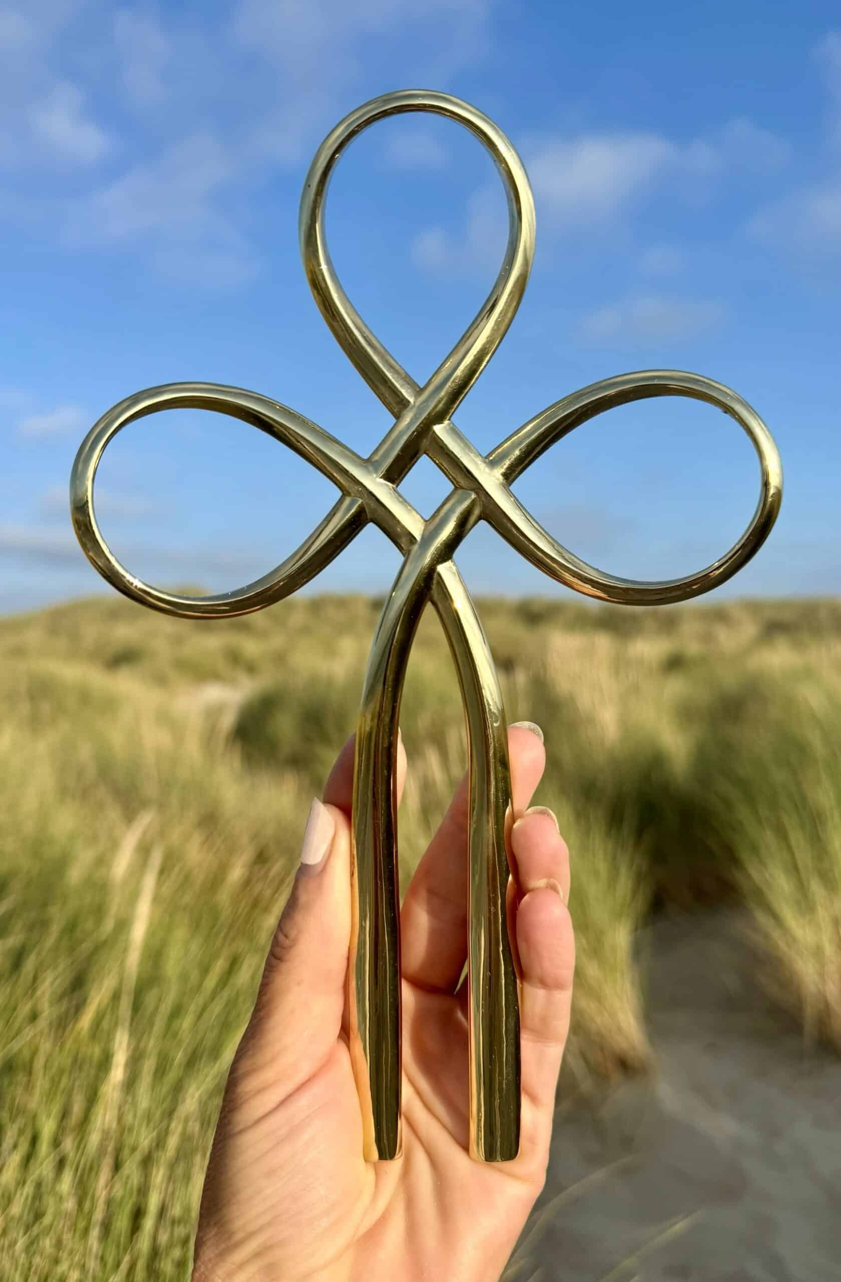 Hand houdt een gouden symbool van Kundalini in een open veld onder een blauwe hemel.