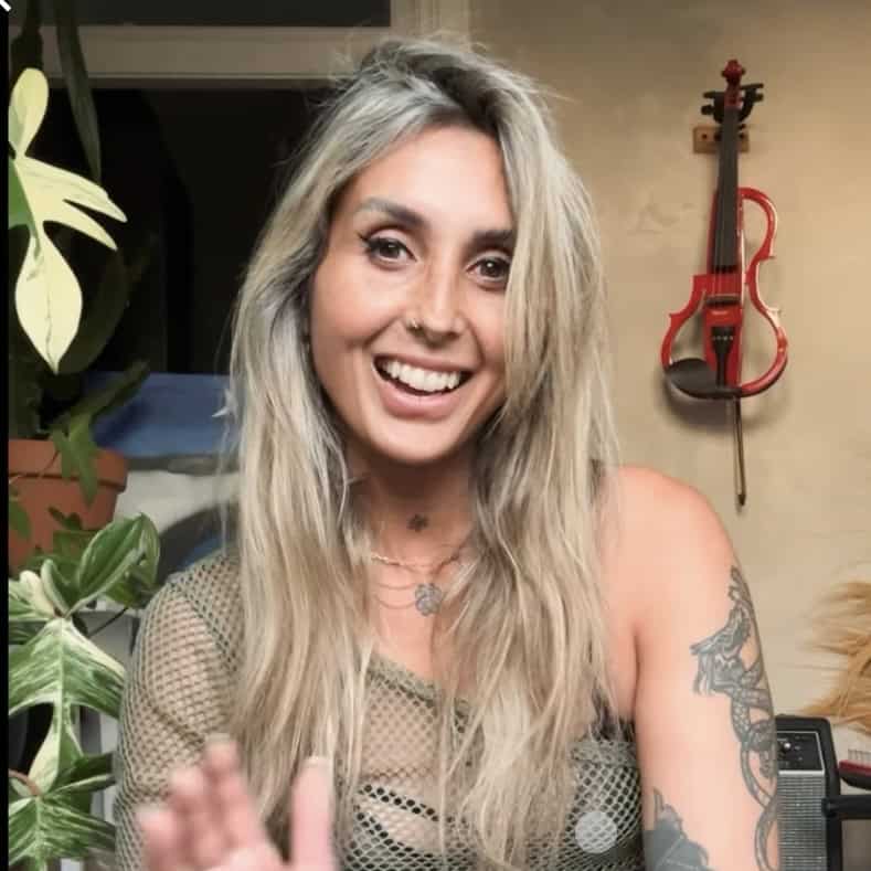 Vrolijke vrouw met lang blond haar en tattoos, in een gezellige kamer.